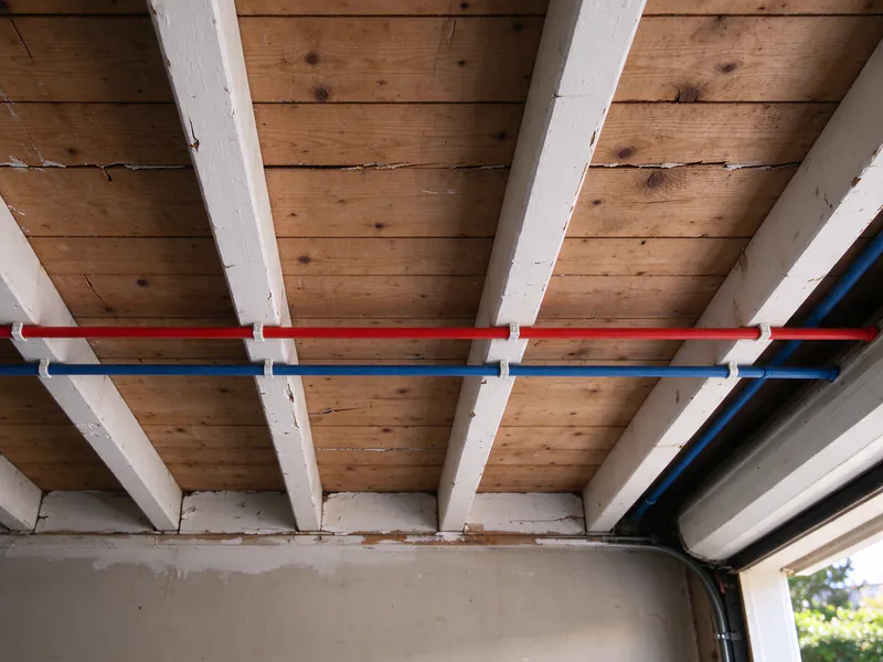 New red and blue PEX trunk lines clipped across the joists of a San Francisco garage ceiling