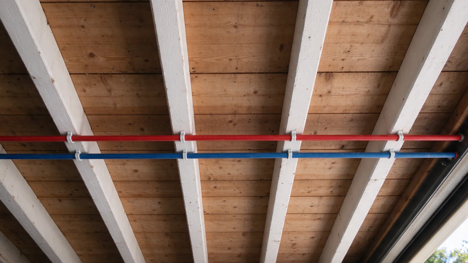 Red and blue PEX lines clipped to garage joists