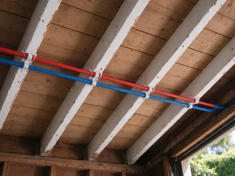 Red and blue PEX lines clipped in parallel across the joists of a San Francisco garage ceiling