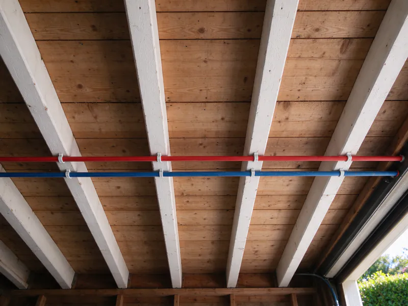 Red and blue PEX trunk lines clipped across the joists of a San Francisco garage ceiling